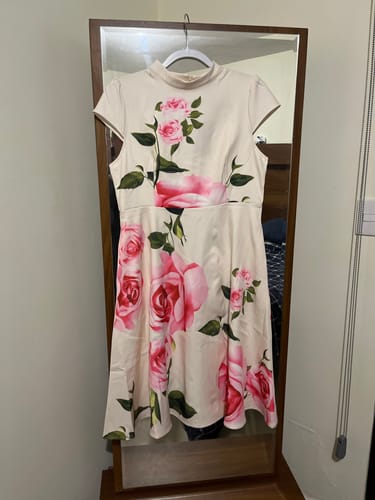 Customer's cream-colored dress with a pink floral print and mock-neck hanging on a hanger.