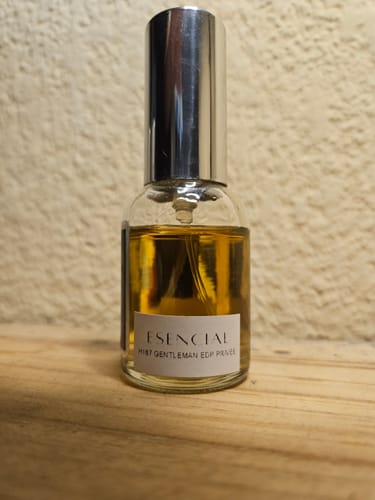 Frasco del perfume H167 de un cliente, con líquido de color ámbar y tapa plateada sobre una superficie de madera.