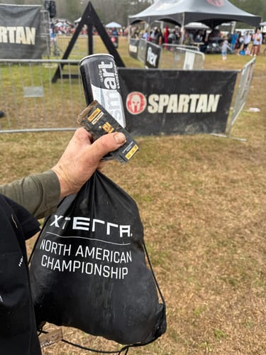 Customer holding a muddy SuperCharged Honey packet and a drink at an outdoor race event.