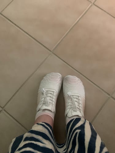 Customer's top-down view of their white Lorax Pro barefoot shoes worn with zebra-print pants.