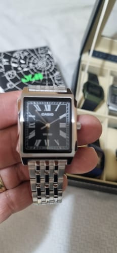 Un cliente sostiene el Reloj Casio Tank Análogo, mostrando su esfera negra y su correa de acero inoxidable.