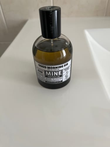 Il flacone di profumo GOODMORNING SIR di un recensore appoggiato su una mensola bianca del bagno.