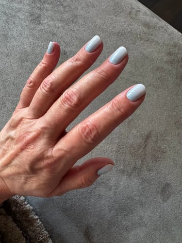 Eine Kundin zeigt ihre Maniküre mit den Babyboomer Sky Nagelfolien, die einen schönen, hellblauen Verlauf haben.