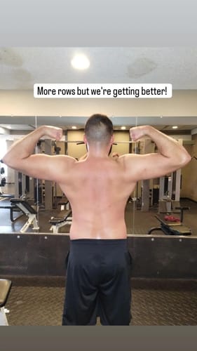 Customer flexing their muscular back and biceps in a gym mirror, showing their progress.