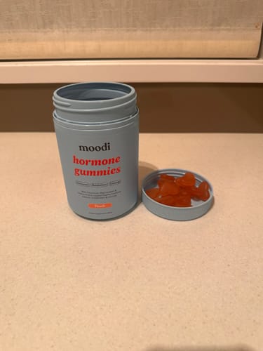 Customer's open blue jar of Moodi Hormone Gummies, with several peach-flavored gummies in the lid.