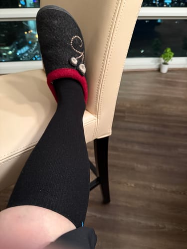 Customer wearing a black Performance Eucalyptus Compression Sock while resting their leg on a chair indoors.