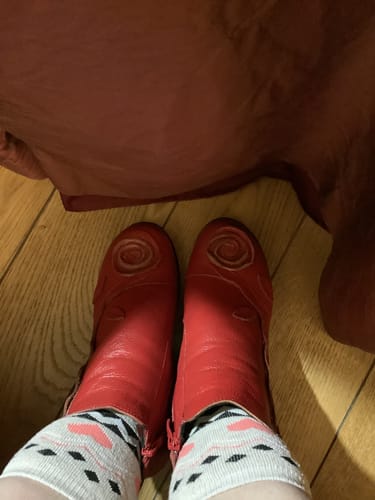 Reviewer's top-down view of the red Retro Flower Leather Boots worn on a wooden floor.
