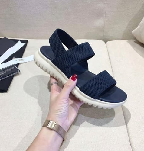 Customer holding a navy Essence sandal, showing the soft crossover straps and thick white sole.