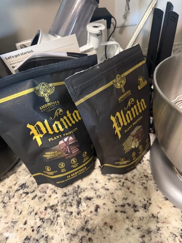Customer's two black bags of Planta plant protein powder on a kitchen counter next to a stand mixer.