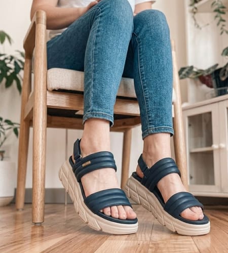 Customer sitting indoors wearing the dark blue The Align sandals, showing the padded straps.
