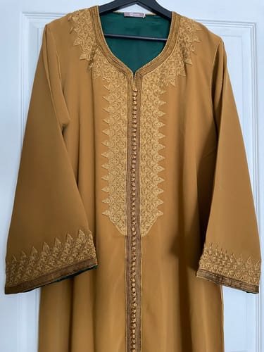 Reviewer's warm mustard Muna kaftan on a hanger, showing its elegant embroidery on the chest and sleeves.
