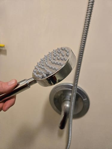 Customer holding the chrome 1-Spray Handheld Shower Head, showing its silicone nozzles.