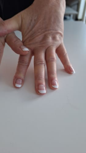 Nahaufnahme der Hand einer Kundin, die ihre elegante „Classy French“ UV Gel-Maniküre auf einem weißen Tisch zeigt.