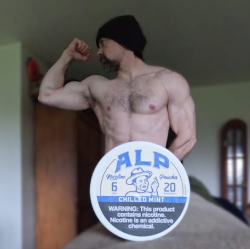 A muscular reviewer flexes their arm, posing behind a large can of ALP Chilled Mint nicotine pouches.