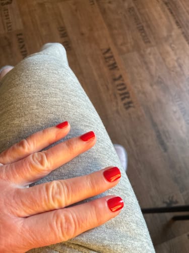 Hand einer Rezensentin mit den glänzend roten 'Hot Date' UV-Gel-Nagelfolien auf kurzen Nägeln.