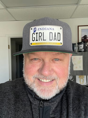 Reviewer smiling while wearing a grey Indiana Plate Hat with a custom license plate patch that reads 'GIRL DAD'.