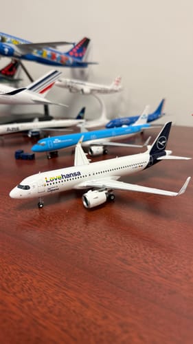 Reviewer's Lufthansa A320neo Lovehansa model plane on a wooden desk with other model planes blurred in the background.