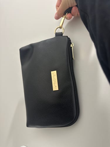 Reviewer holding the black Tech Pouch by its wrist strap, showing the gold hardware.