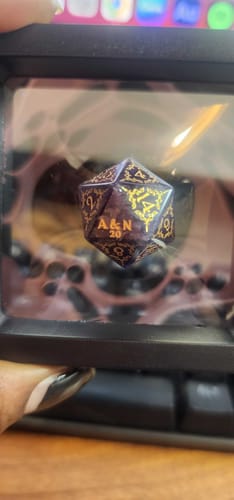 Customer's custom purple D20 die in a clear box, showing the personalized 'A & N' engraving on the 20 face.