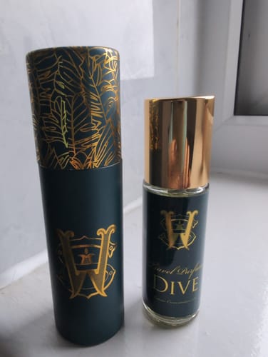 Customer's travel size perfume atomiser next to its decorative green and gold tube case.