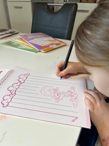 Kundenrezension: Ein Kind schreibt in einem offenen Edubini Magischen Übungsheft auf einem Tisch.