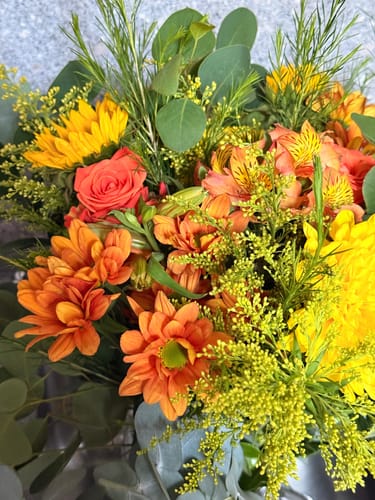 Close-up of a customer's vibrant Sparkling Orange Bouquet, with a mix of fresh orange, yellow flowers and green foliage.