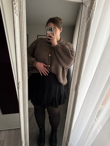 Rezensentin zeigt den braunen Oversized-Cardigan 'CozyGlam' und den schwarzen Rock 'Summer' in einer Spiegelaufnahme.