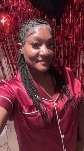 Customer wearing a black wig styled in intricate braids over one shoulder against a festive red background.