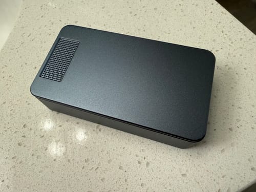 Customer's dark grey metal pill case from the bundle, shown closed on a white countertop.