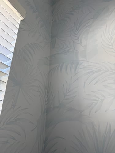 Close-up of reviewer's Coastal Luxe Palms Wallpaper in duck egg blue installed in a room corner.