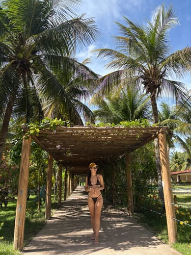 Cliente usando o Top Fita Marrom Coffee em um caminho tropical com palmeiras ao fundo.