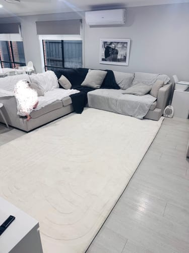 Customer's large Vanilla Cream Mellow Mat in their living room, placed in front of a grey sofa.