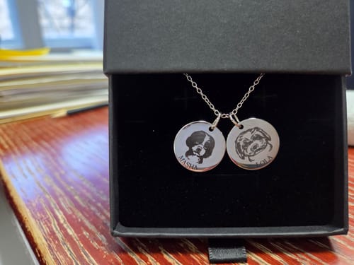 Customer's silver Pet Portrait Necklace with two round pendants engraved with dogs, shown in a black gift box.