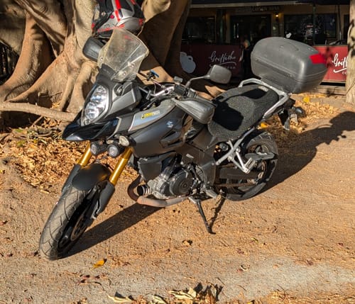 Customer's black Wind Rider Seat Cover installed on a motorcycle parked on a dirt path.