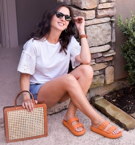 Reviewer styling the orange Vibe platform sandals while sitting on a stone step outdoors.