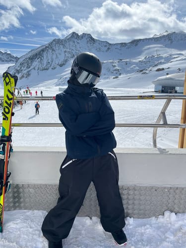 Reviewer on a snowy mountain slope, wearing the baggy black snow pants with a helmet.