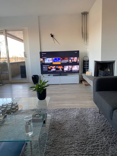 Klant toont de NeXtime Hands wandklok in een modern interieur, hangend boven de televisie.