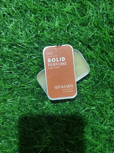 Customer's open tin of Ispahan Solid Perfume resting on a patch of bright green grass.