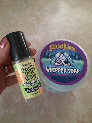 Customer holding the small Deadly Dole Whip Perfume Oil bottle next to a tub of whipped soap.