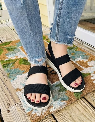 A reviewer wearing the black Essence sandals with thick white soles, paired with cuffed blue jeans.