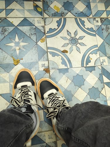 Customer's first-person view of their multicolor Bacca Bucci Urban Genesis 1.0 sneakers on a patterned tile floor.