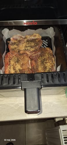 Recenzent arătând carnea crudă, condimentată, în cuva air fryer-ului Novio StonePro, gata de gătit.
