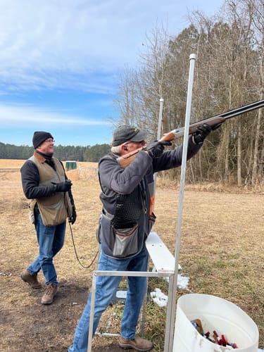 Reviewer at a shooting range aiming a shotgun while wearing the XCOR Digital Exchange buds for hearing protection.