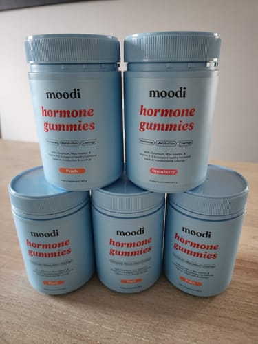 Reviewer's five blue tubs of Original Hormone Gummies in peach and strawberry flavors stacked on a wooden table.