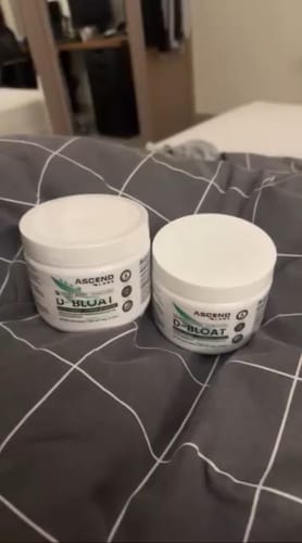 Customer's two white tubs of D-BLOAT powder sitting side-by-side on a grey checkered bedspread.