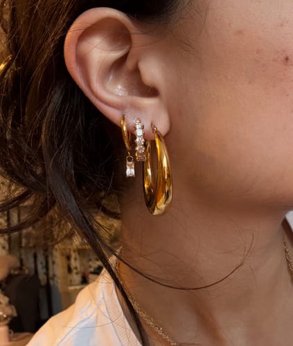Nahaufnahme des Ohrs einer Kundin, die den Simple Baguette Ohrring mit anderen goldenen Ohrringen kombiniert.
