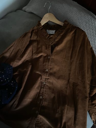 Image d'une cliente de la blouse Miléna en velours camel, présentée sur un cintre en bois.