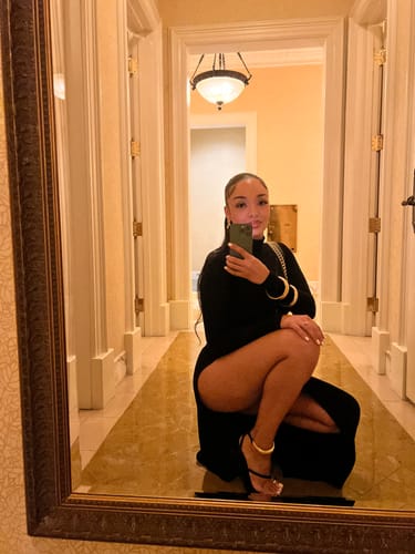 Reviewer crouching to showcase the high slit on the black Butter Contour High Slit Maxi Dress.