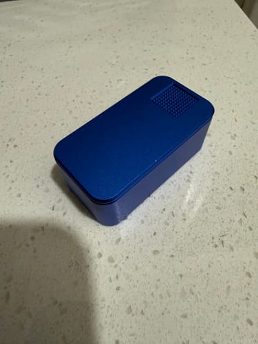 Customer's blue metal pill case with a textured lid, shown on a speckled countertop.