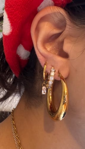 Nahaufnahme des Ohrs einer Kundin, die die großen, goldenen Lucia Ohrringe trägt.